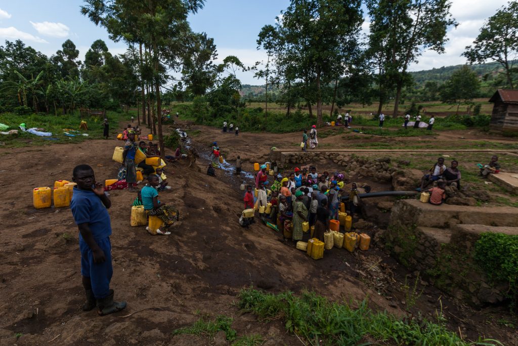 A large group of people collecting water from a shared source in a rural community in the DRC, highlighting water scarcity and infrastructure challenges.