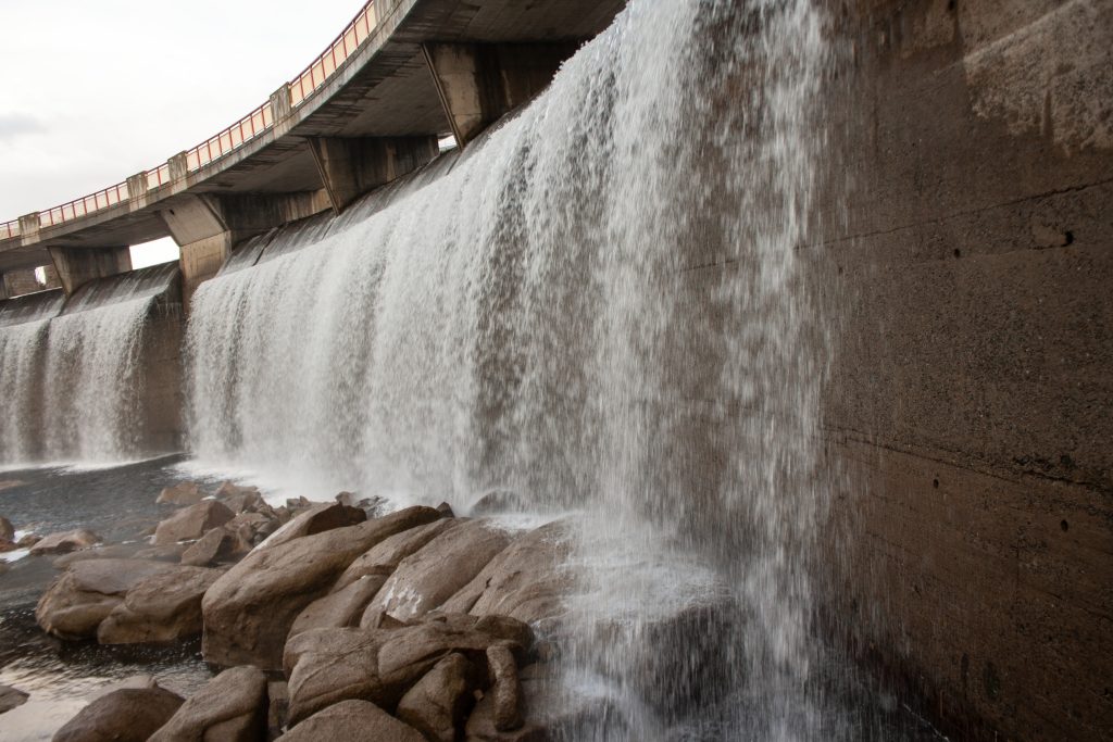 Water cascading from the spillway of a concrete dam, representing critical infrastructure vulnerability and physical security risks.