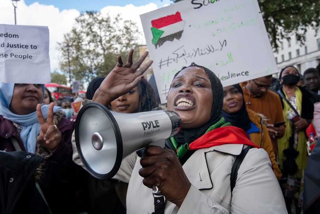 A Sudanese woman speaks through a megaphone at a protest, reflecting the strength and determination of civilian movements for justice and democratic rule.