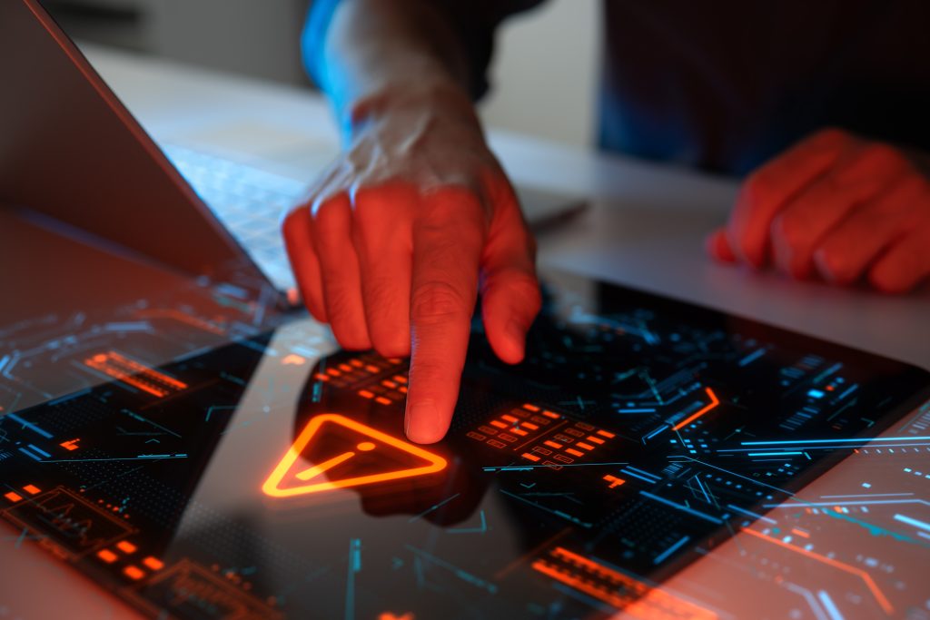 A hand interacting with a touchscreen cyber alert interface, symbolising cybersecurity threats, system vulnerabilities and digital risk detection.
