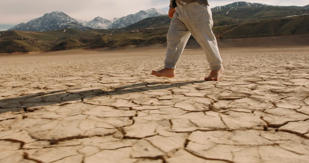 Child walking across cracked, drought-stricken ground with mountains in the background, illustrating climate change and environmental stress