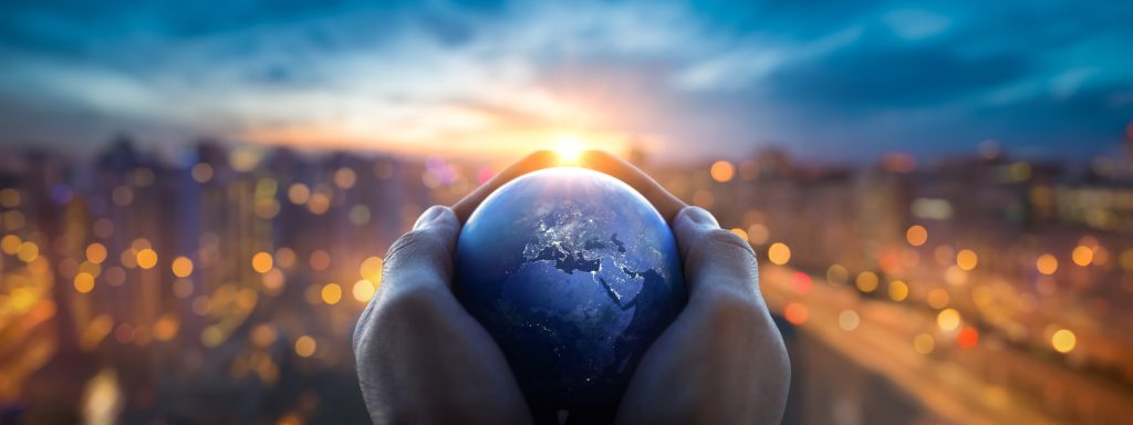 Hands holding a globe against a city skyline at sunset, representing global governance, shared responsibility, and international cooperation