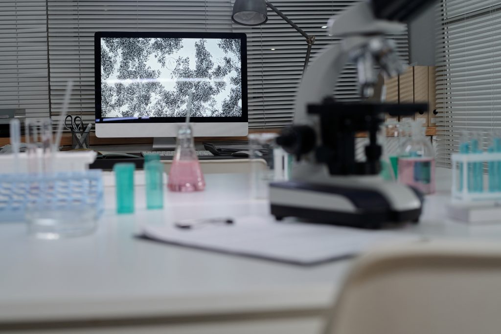 Laboratory workspace with microscope, test tubes, and digital analysis screen used in synthetic biology research and bioengineering