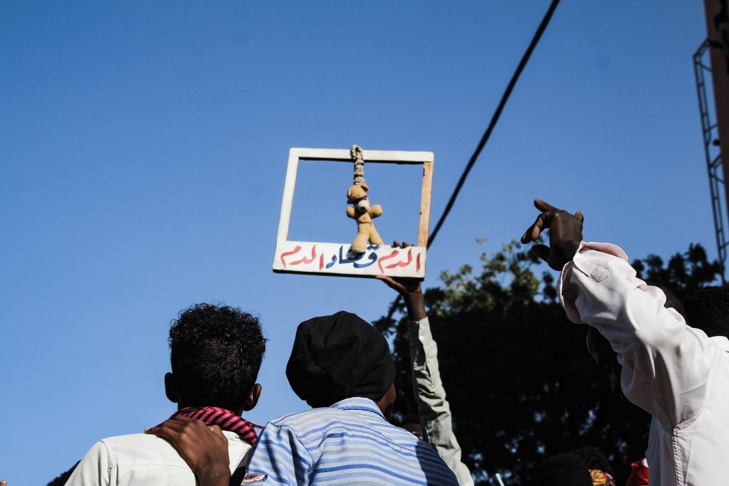 Sudanese civilians protesting war and violence, holding symbolic sign highlighting humanitarian crisis in Sudan