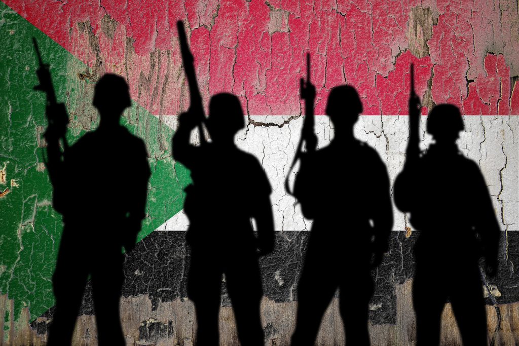 Silhouettes of armed fighters against Sudan flag symbolising military fragmentation and armed groups in the Sudan civil war