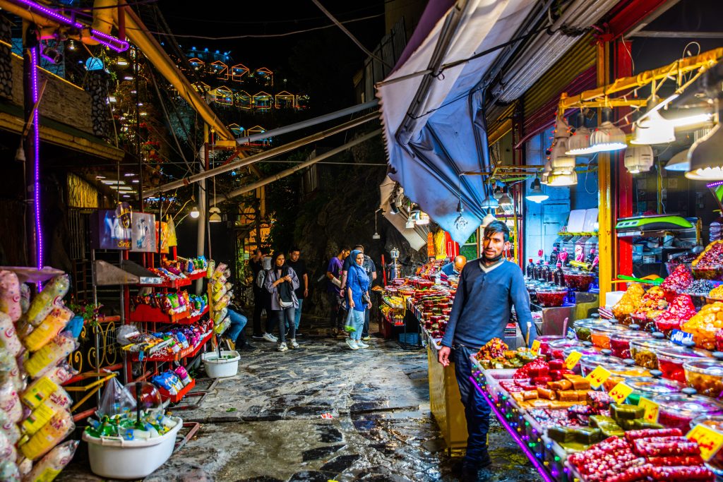 Vibrant Iranian street market at night with colourful food stalls and shoppers, reflecting everyday economic life amid inflation and currency instability in Iran