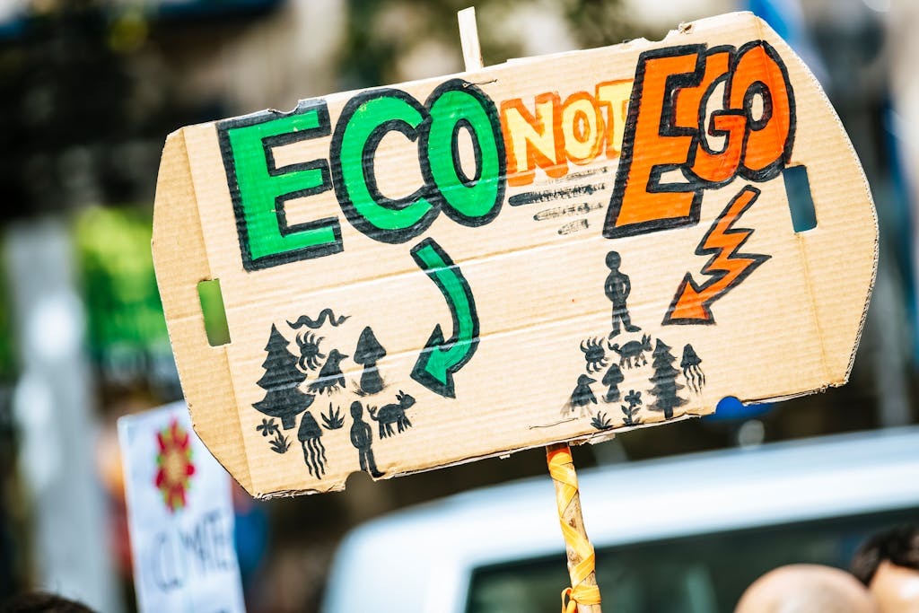 Close-up of a cardboard protest sign with 'Eco Not Ego' message at a climate rally.