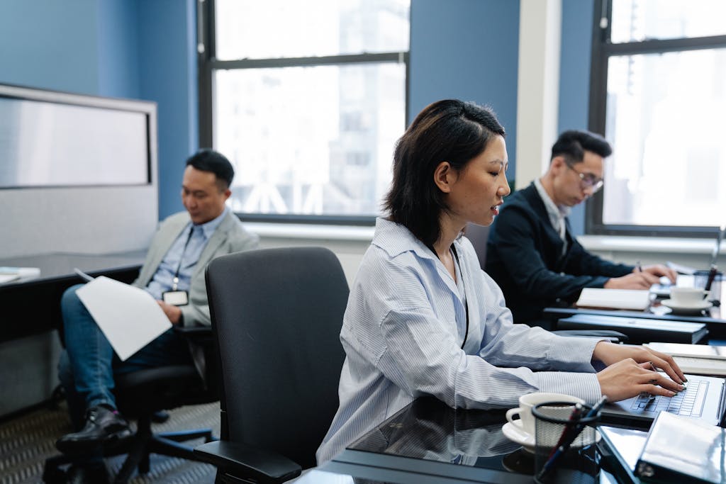 Focused Asian professionals working on laptops in a modern office environment, emphasizing collaboration.