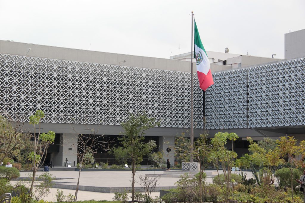 Modern government building in Mexico City with Mexican flag in foreground, representing state institutions and governance