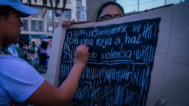 Woman writing on a protest sign during a demonstration against violence in an urban setting.