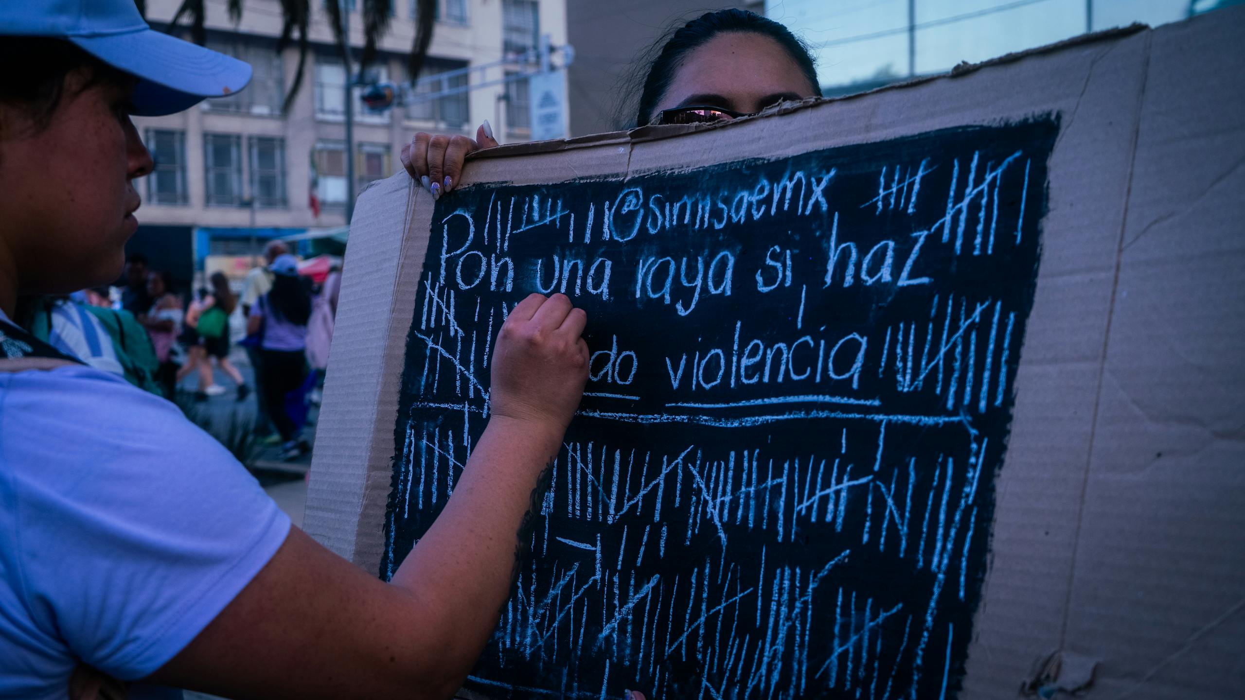 Woman writing on a protest sign during a demonstration against violence in an urban setting.