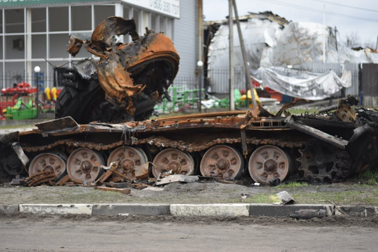 A rusted and damaged military tank lies abandoned on a city street.