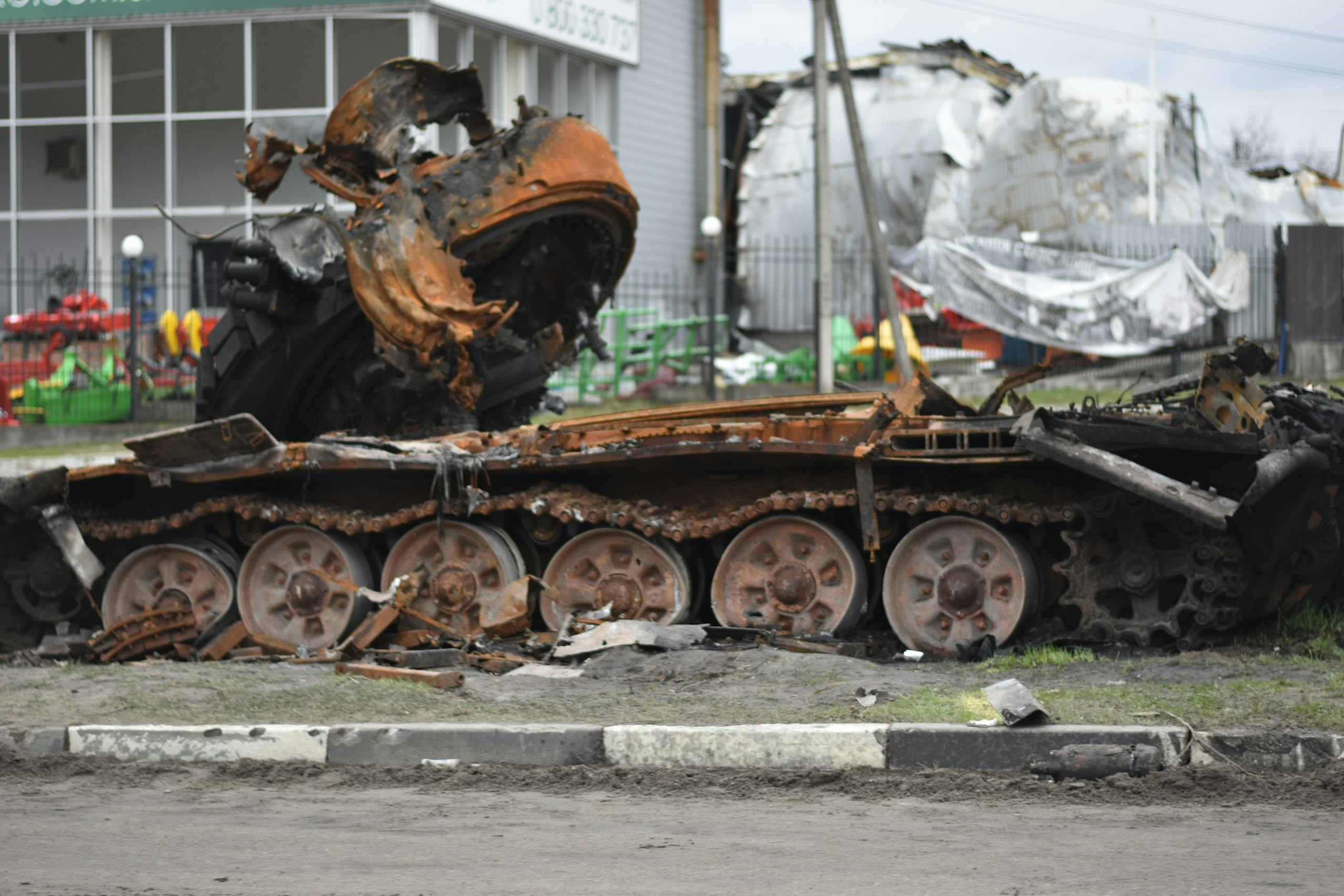 A rusted and damaged military tank lies abandoned on a city street.