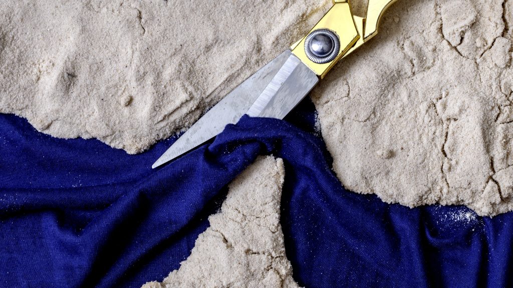Knife cutting fabric in sand symbolising disruption of global trade routes, fractured supply chains, and geopolitical instability