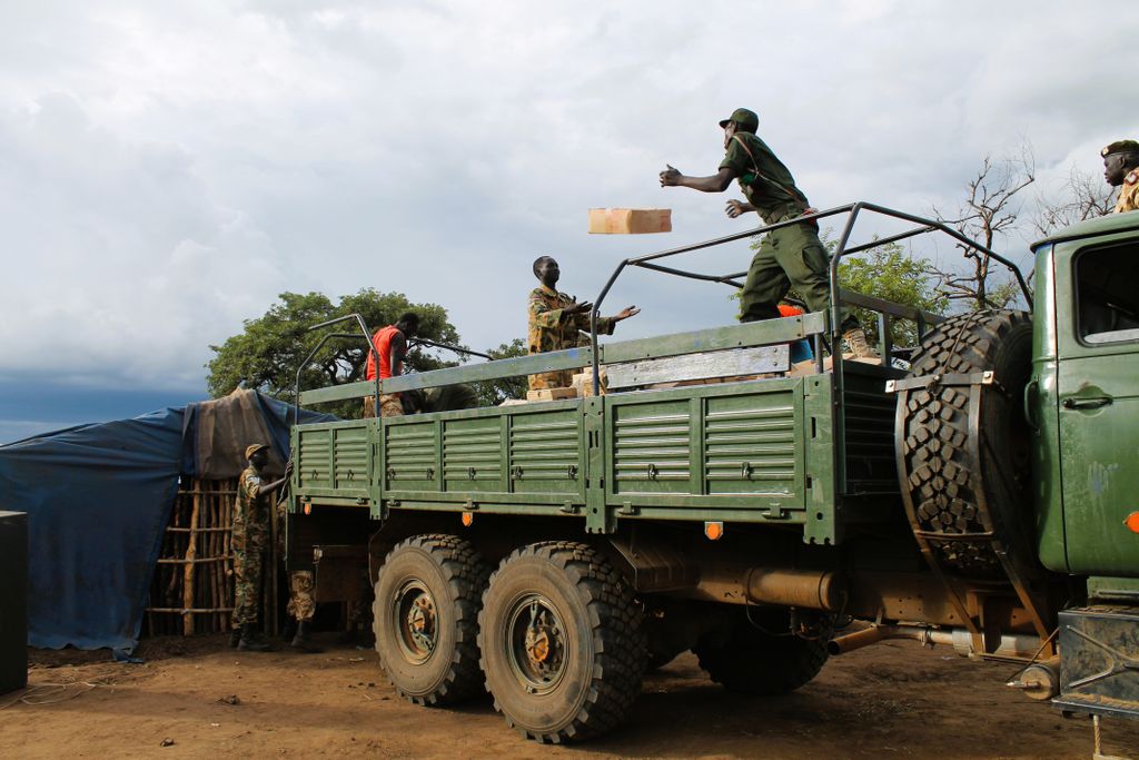 Soldiers in camouflage loading a truck with supplies in an outdoor setting.